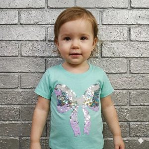 A cute baby girl wearing a mint green t-shirt with a sparkly sequin bow design.