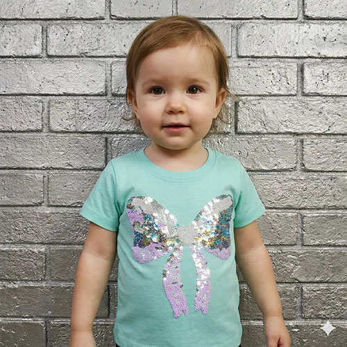 A cute baby girl wearing a mint green t-shirt with a sparkly sequin bow design.